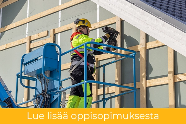 Henkilö henkilönostimella ja naulaa talon ulkoseinää.