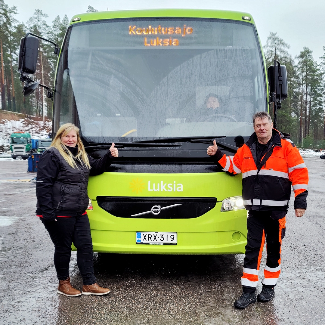 Vihreän linja-auton edessä seisoo kaksi ihmistä peukalot pystyssä.